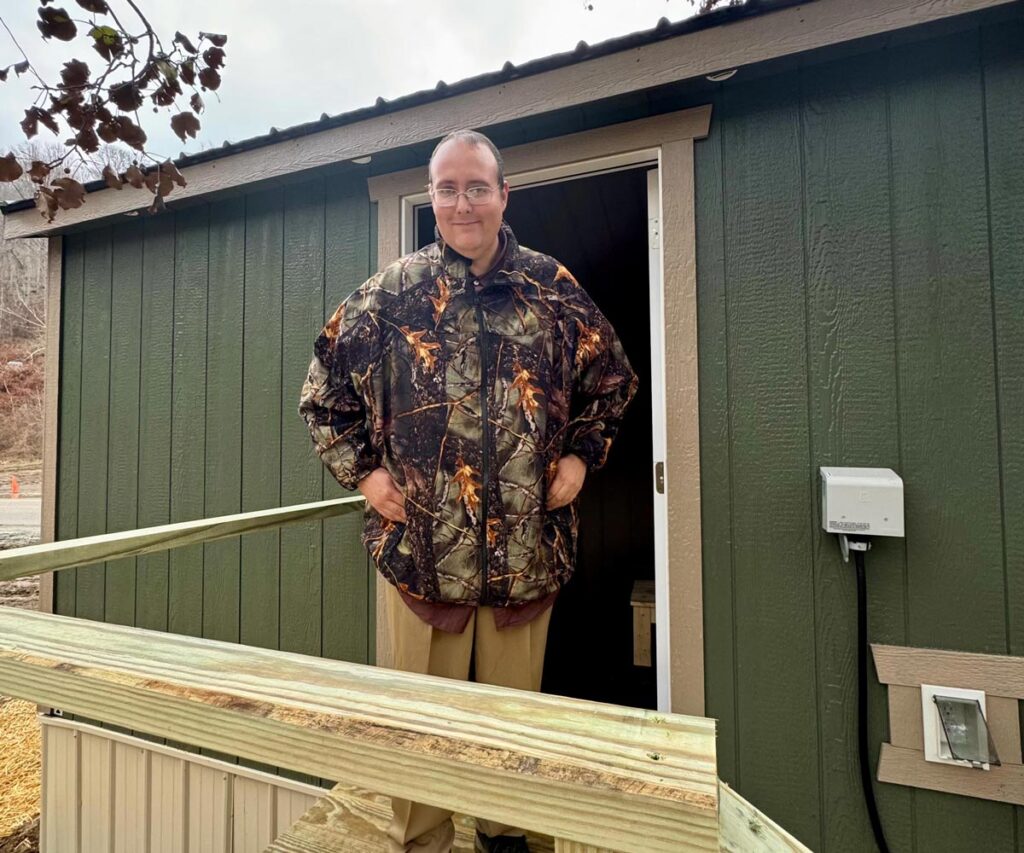 A gentleman smiles as he stands outside the door of his recently delivered tiny home 